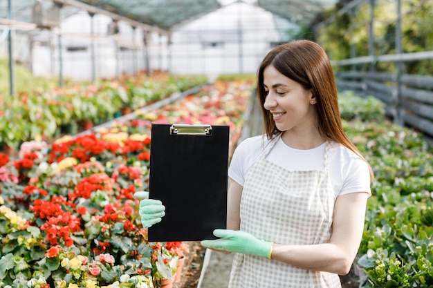 Portret van tuinman vrouw aan het werk in kas met notitieboekje onderzoekt de groeiende bloemen in kas Thuis tuinieren liefde voor planten en zorg Klein bedrijf