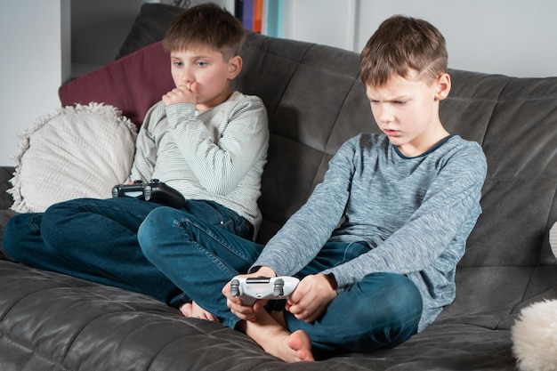 Portret van twee boze, verontwaardigde tienerjongens die thuis op de bank zitten met een joystick die videogames speelt en het spel verliest