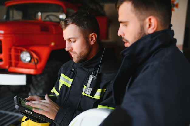 Portret van twee brandweerlieden in brandbestrijdingsoperatie brandweerman in beschermende kleding en helm met behulp van tabletcomputer in actiegevechten