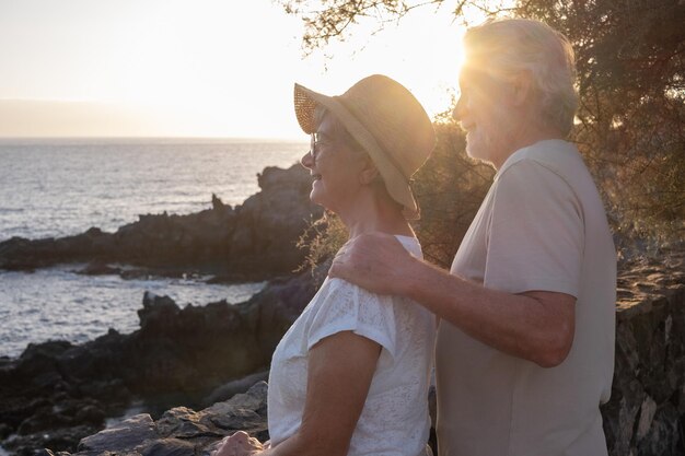 Portret van twee gelukkige en romantische senioren omarmd op zee bij zonsondergang genietend van vakanties