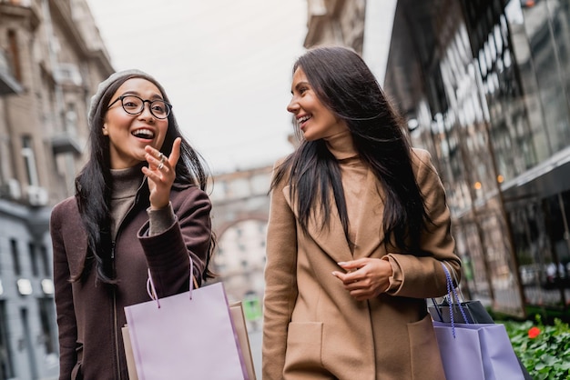 Portret van twee gelukkige vrouwen met boodschappentassen die wijzen terwijl ze samen door de straten van de stad lopen