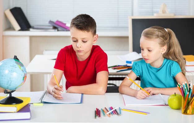 Portret van twee ijverige meisjes die naar de camera kijken op de werkplek met schooljongens op de achtergrond