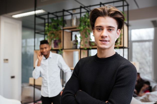 Portret van twee jonge knappe studenten in bibliotheek. Blanke man kijkt naar boek. Afrikaanse jongen staande praten via mobiele telefoon.