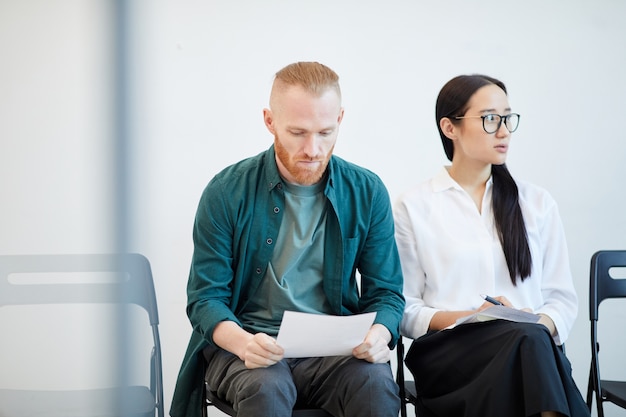 Portret van twee jonge mensen die in de rij wachten op sollicitatiegesprek en notities bekijken, kopie ruimte