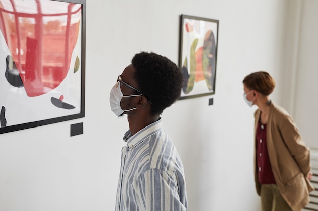 Portret van twee jonge mensen die naar schilderijen kijken terwijl ze maskers dragen op de tentoonstelling van moderne kunstgalerieën,