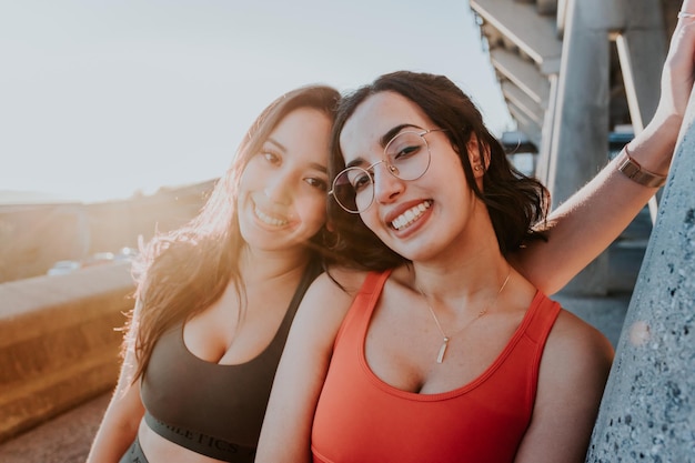 Portret van twee jonge sportieve meisjes die naar de camera glimlachen terwijl ze rusten na het joggen tijdens een zonsondergang. uitwerken van kleding, top en legging, afrikaanse vrouw fitness. sunset ambient, slanke lichamen.