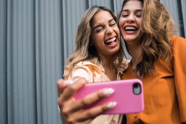 Portret van twee jonge vrienden die samen plezier hebben en buitenshuis een selfie met een mobiele telefoon nemen. Stedelijk concept.