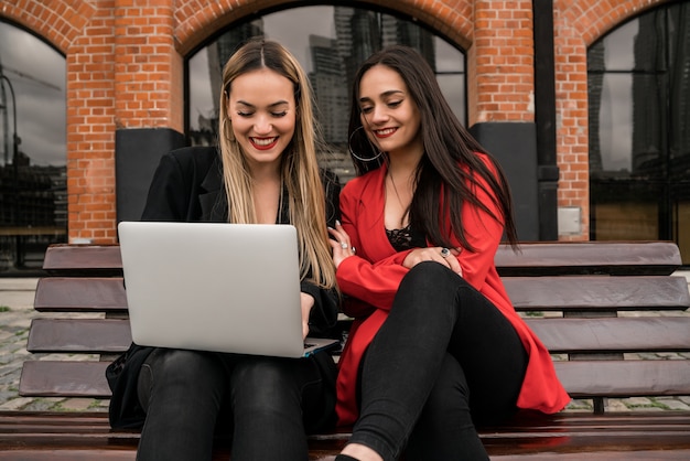 Portret van twee jonge vrienden met behulp van een laptop zittend buiten