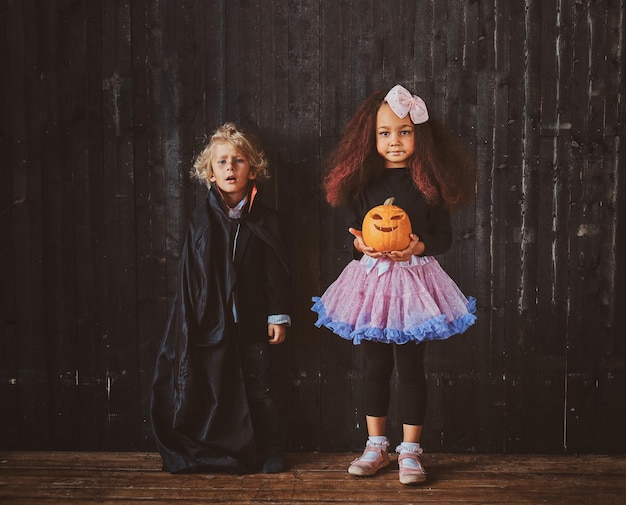 Portret van twee kinderen in Halloween-kostuums over donkere achtergrond.