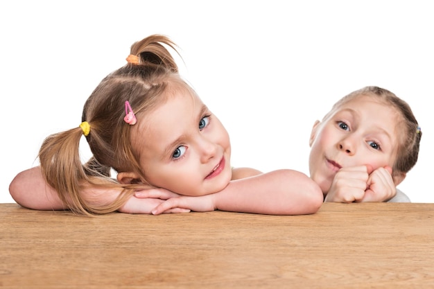 Portret van twee kleine meisjes die aan de tafel zitten en erop staan geïsoleerd op een witte achtergrond