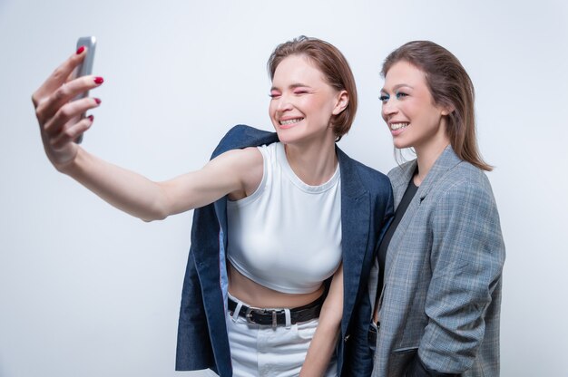 Portret van twee lachende vrouwen in blazers die een selfie maken. vriendschapsconcept. gemengde media