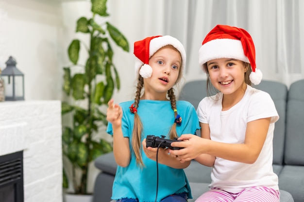 Portret van twee leuke lieve mooie mooie aantrekkelijke charmante grappige vrolijke positieve meisjes in kerstmutsen die op divan zitten en videoapparaatgevecht spelen