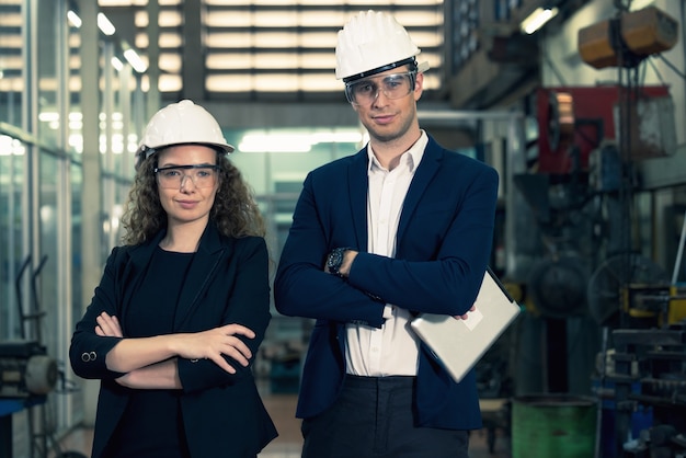 Portret van twee machinisten staat met een veiligheidshelm vol vertrouwen voor de glazen wand van de industriefabriek.