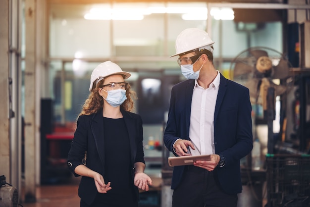 Portret van twee machinisten staat met tablet en veiligheidshelm voor de glazen wand van de industriefabriek.