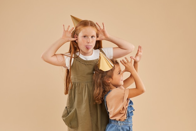 Foto portret van twee meisjes die grappige gezichten maken terwijl ze op beige poseren