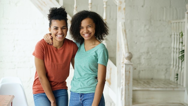 Portret van twee mooie Afro-Amerikaanse meisjes die lachen en thuis in de camera kijken