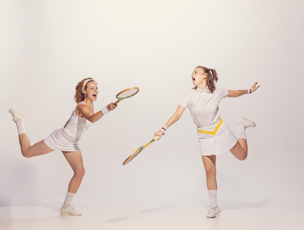 Portret van twee mooie jonge vrouwen in retro uniform die badminton spelen geïsoleerd over grijze studio