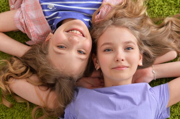 Portret van twee mooie kleine meisjes die op een groen tapijt liggen en naar de camera kijken