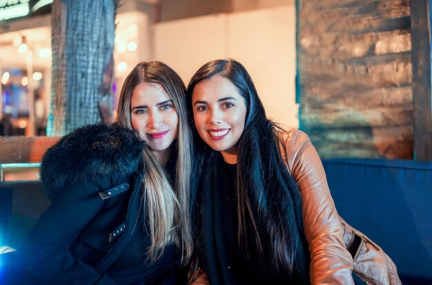 Portret van twee mooie latijnse vrouwen die 's nachts in een pub of restaurant zitten