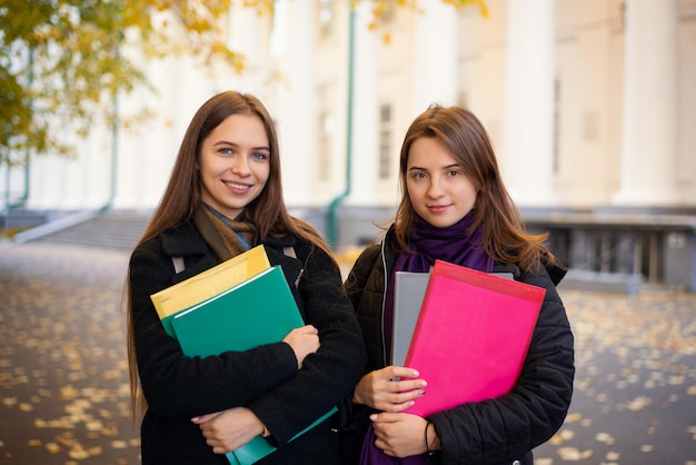 Portret van twee mooie meisjesstudenten dichtbij universiteitsgebouw bij het concept van het Herfstonderwijs