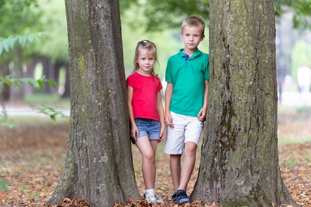 Portret van twee mooie schattige kinderen jongen en meisje permanent in de buurt van grote boomstam in zomer park buitenshuis.