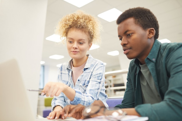 Foto portret van twee studenten, kaukasisch meisje en afrikaanse jongen, wijzend op laptopscherm tijdens het werken