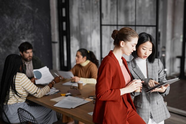 Portret van twee succesvolle zakenvrouwen die communiceren terwijl ze aan de vergadertafel in het kantoorinterieur staan, kopieer ruimte