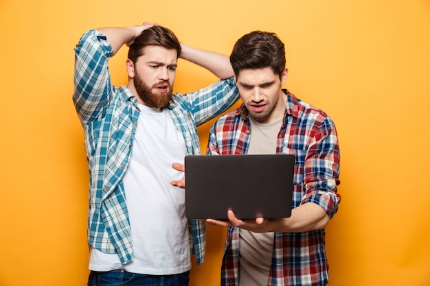 Portret van twee verstoorde jonge mannen die laptop met behulp van