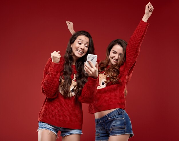 Portret van twee vrij gekke beste vrienden in mode gezellige winter trui schreeuwen van vreugde tijdens het kijken naar de telefoon