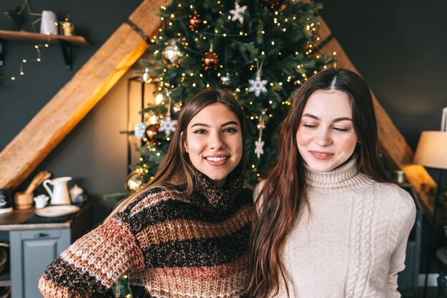 Portret van twee vrolijke jonge kaukasische vrouwenvriend dichtbij kerstboom.
