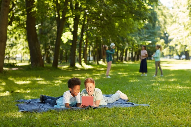 Portret van twee vrolijke jongens met behulp van digitale tablet liggend op groen gras in park buiten verlicht door zonlicht