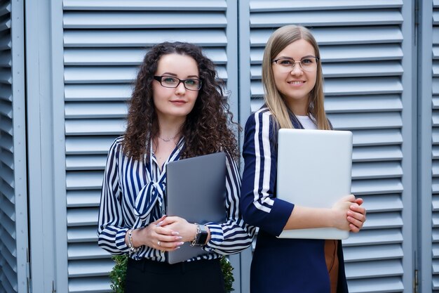 Portret van twee vrouwelijke zakenlieden die met laptops in hun handen staan, nieuw project. jonge zakelijke collega's bespreken kantoorwerk. succesvolle vrouwelijke manager met een bril. bedrijfsconcept