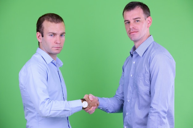 Foto portret van twee zakenlieden die handen samen tegen groen schudden