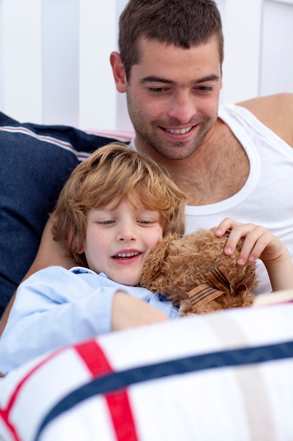 Portret van vader en zoon die een boek in bed lezen