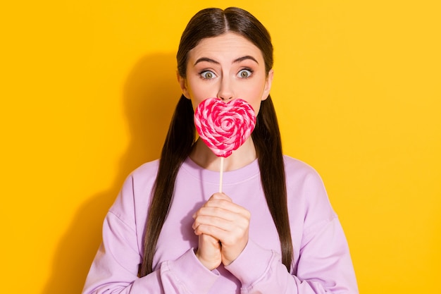 Portret van verbaasd grappig meisje sluit lippen met smakelijke hartvormige snoep
