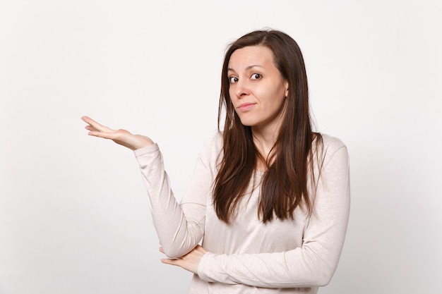 Portret van verbijsterde verbaasde jonge vrouw in lichte kleding op zoek naar camera, wijzende hand opzij geïsoleerd op een witte achtergrond in de studio. Mensen oprechte emoties, lifestyle concept. Bespotten kopie ruimte.