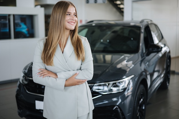 Portret van verkoper in autoshowroom, aantrekkelijke jonge vrouw die voor de auto staat