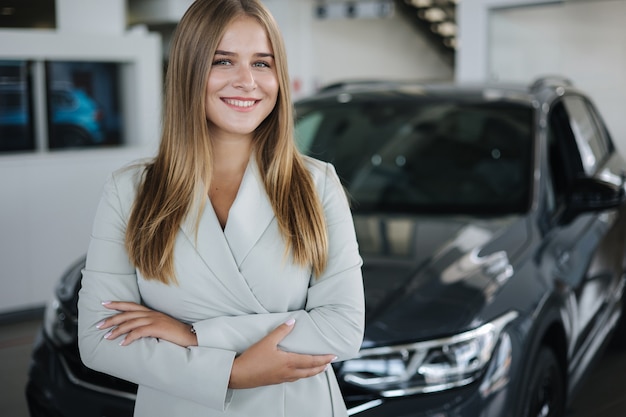 Portret van verkoper in autoshowroom, aantrekkelijke jonge vrouw die voor de auto staat