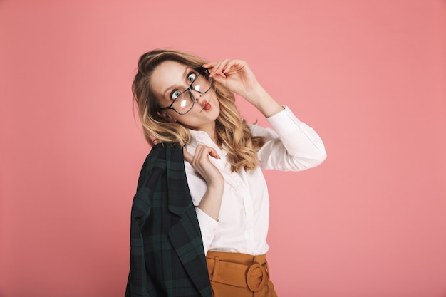 Portret van verleidelijke blonde vrouw 30s in stijlvolle outfit aanraken van brillen geïsoleerd op rood