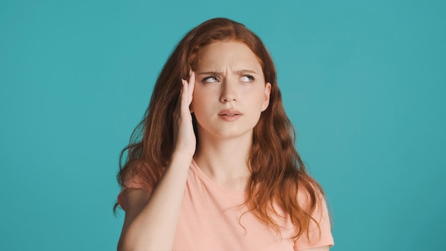 Portret van vermoeid roodharig meisje dat hoofdpijn op camera toont over kleurrijke achtergrond