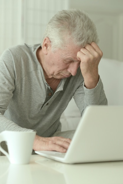 Portret van vermoeide senior man in de keuken thuis met laptop