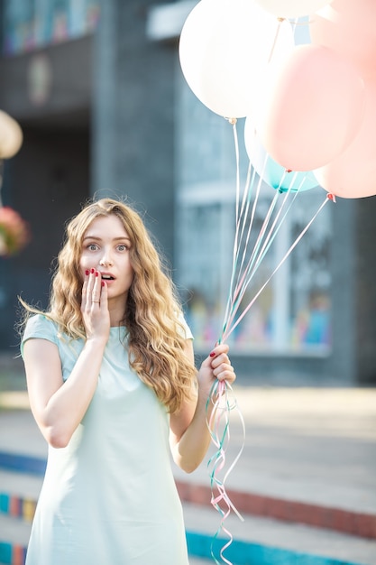 Portret van verrast mooie vrouw met vliegende veelkleurige ballonnen in de stad