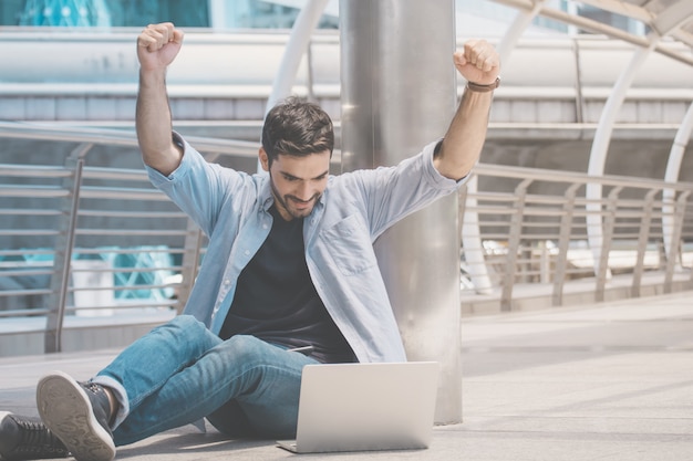 Portret van verraste knappe man zittend op de vloer met laptop. Succes zaken.