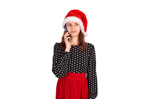 Portret van verwarde jonge dame in kleding die op haar telefoon spreekt. emotioneel meisje in de geïsoleerde Kerstmishoed van de Kerstman