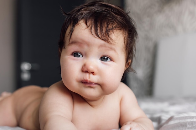 Portret van verwarde naakte baby liggend op bed deken thuis onscherpe achtergrond baby kind kruipen op buik in slaapkamer close-up verkennen wereld Selectieve focus gratis kopie ruimte Kinderopvang concept