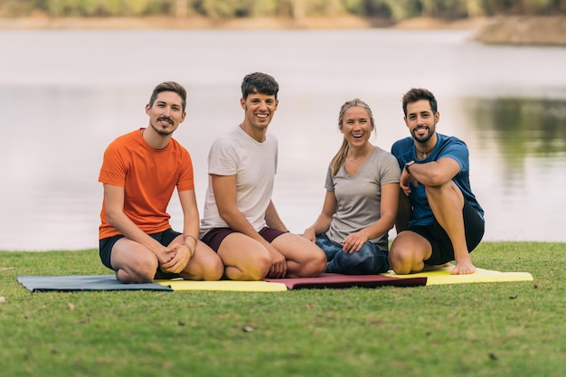 Portret van vier mensen die naar de camera kijken terwijl ze op een yogamat in een park zitten