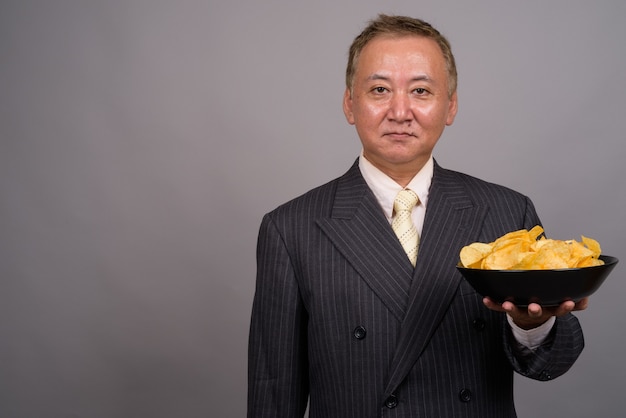 Portret van volwassen Aziatische zakenman tegen grijze muur