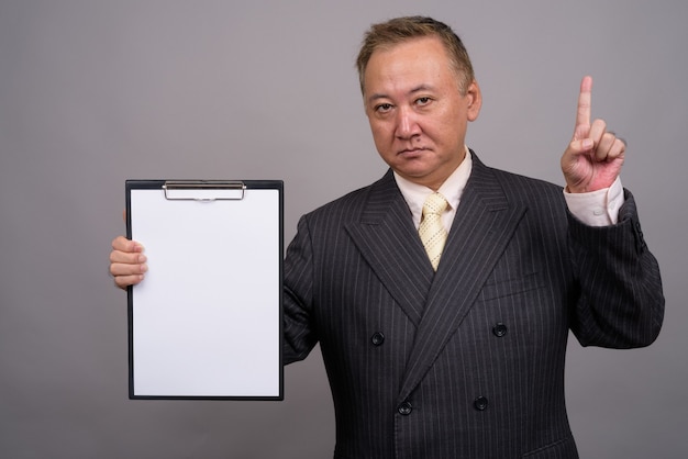 Portret van volwassen Aziatische zakenman tegen grijze muur