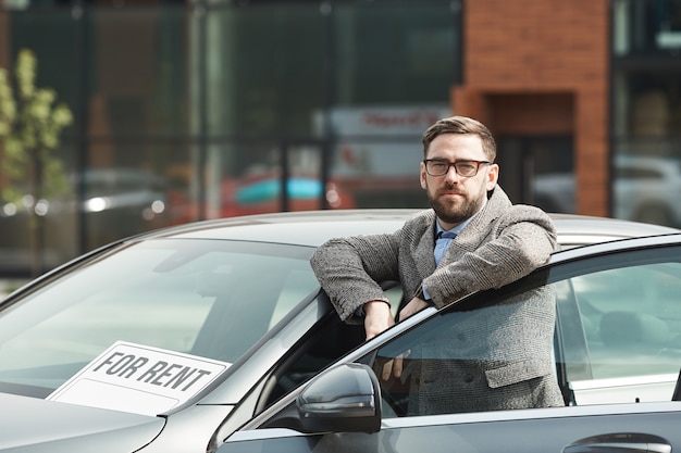 Portret van volwassen bebaarde zakenman in brillen terwijl hij in de buurt van de auto buiten staat