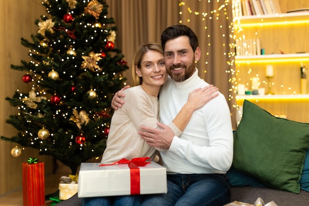 Portret van volwassen familie bebaarde man en blonde vrouw kijken camera knuffelen in de buurt van kerstboom